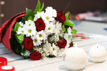 A beautiful bouquet of red roses and Chamomile lies. Candles, holiday