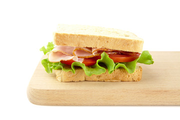 Sandwich with lettuce,tomato,cold cuts on cutting board on white