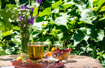 cup of green tea on a table with fruits and flowers in the garden