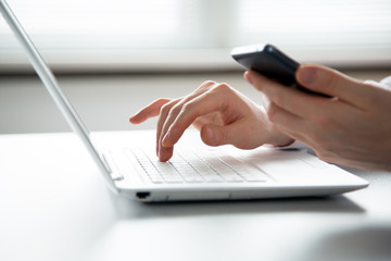 Businessman holding phone and using laptop.