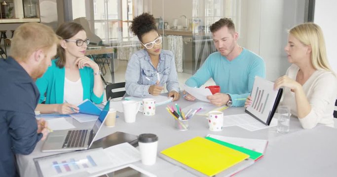 Side view of woman holding folder with document and showing it to coworkers while having conference at table in modern office.