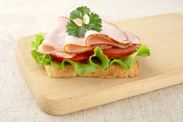 Toast,lettuce,tomato,cold cuts on cutting board on flax tableclo