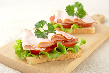 Toasts,lettuce,tomato,cold cuts on cutting board on linen tablecloth