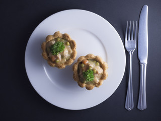 Savory Danish tartlets (tarteletter) made from puff pastry, filled with a creamy chicken, asparagus and carrot sauce. Placed on white plate and isolated on black background