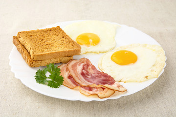 Slice of bacon with two eggs on the plate with toasts