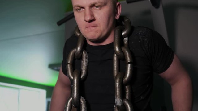 Athlete in gym doing exercises on parallel bars with chain around his neck