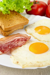 Slice of fried bacon,two eggs on the plate with toasts for breakfast