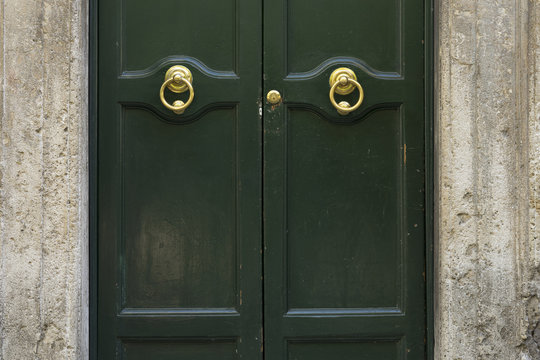 Old metal door handle on a green wooden door. Art work. Rome, It