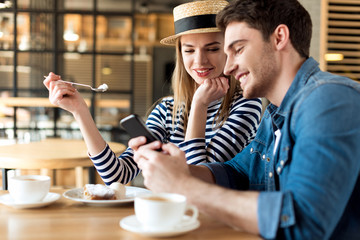 portrait of young couple using smartphone while sitting together in cafe