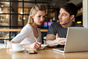 young couple working on laptop together while sitting at table in cafe