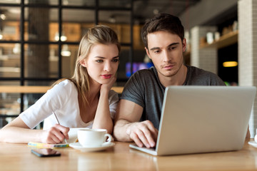 young couple working on laptop together while sitting at table in cafe