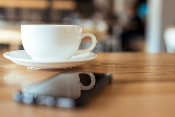 selective focus of cup of coffee on saucer standing on wooden table in cafe