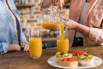 two women, senior and young drinking orange juice at table in kitchen. Woman pouring juice into glass