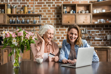 Portrait of two women, senior and young using laptop and credit card doing online shopping