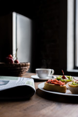Still life of newspaper, breakfast with cakes and hot coffee on kitchen table in front of window