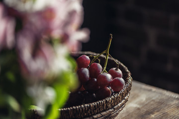 Close-up basket of red grapes on kitchen table and blurred flowers in foreground