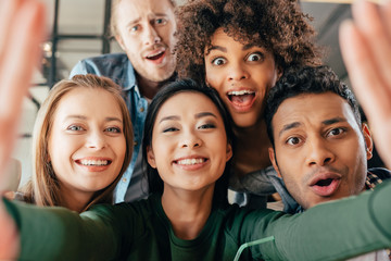 Young happy multiethnic friends taking selfie in cafe