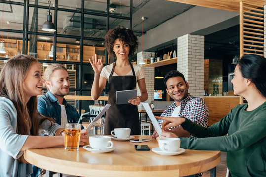 Young African American woman waitress taking orders from clients in cafe