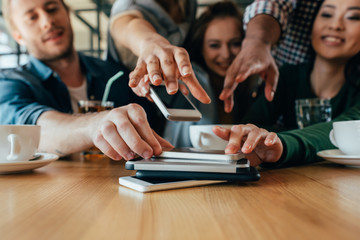 Young friends taking back their smartphones lying in pile on table in cafe