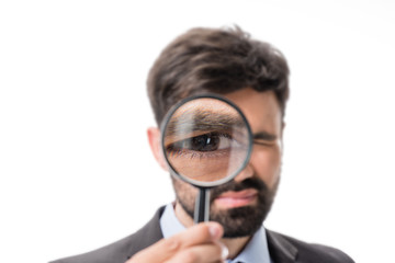 portrait of businessman looking at camera through magnifying glass isolated on white