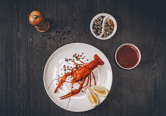 Food concept. Boiled big red fresh crawfish in white plate with lemon slices. Composition with sauce, herbs and pepper grains around. Gray wooden background. Instagram vintage toning effect. Top view.
