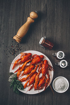 Boiled big red fresh crayfish in white plate with green herbs. Composition with sauce jars and pepper grains around. Gray wooden background. Instagram vintage toning effect. Top view. Copy space.