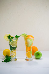 Two cocktail glasses of healthy lemon and mint leaves detox water on white wooden table and white background with lemon and napkin by side. Non-alcoholic mojito or lemonade with ice cubes