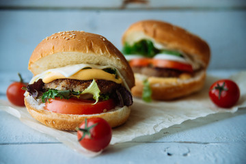 Two hamburgers with beef burger cutlet, fried onion, spinach, ketchup sauce and blue cheese in traditional buns, served on wood chopping board over bright turquoise background. Copy space