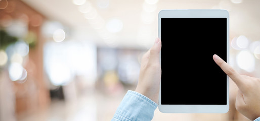Hand using tablet with blank screen for mock up over blur store background