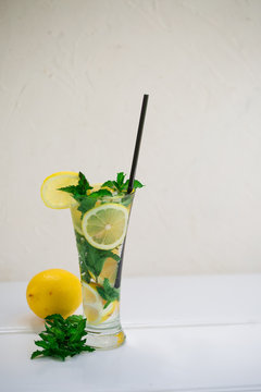 Healthy Lemon And Mint Leaves Detox Water In Cocktail Glass On White Wooden Table With Lemon And Napkin By Side. Non-alcoholic Mojito Or Lemonade With Ice Cubes On White Background