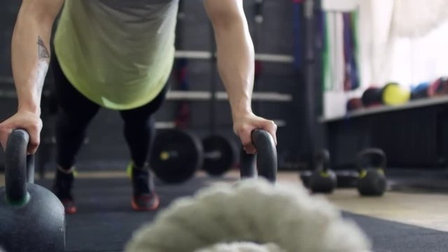 PAN with slow motion of sportswoman with muscular arms leaning on kettlebells and doing push-ups in gym