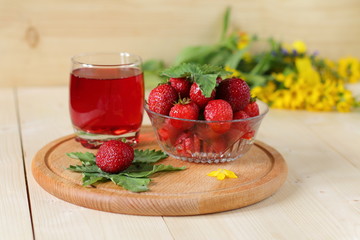 Fresh strawberries and glass of strawberry drink are on a wooden background.