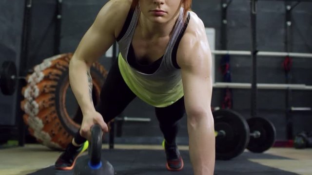 Zoom out of concentrated muscular female athlete doing kettlebell rows with one arm