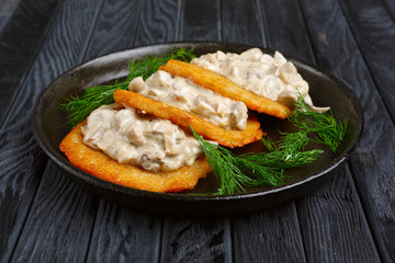 Potato flapjacks (draniki) with onion and mushroom creamy sauce in cast-iron pan
