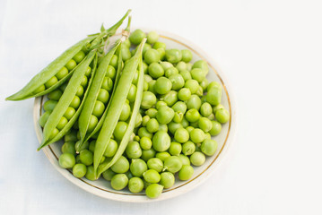 Green pea and pods in a bowl of top view on white background with copy space - healthy food - Flat lay