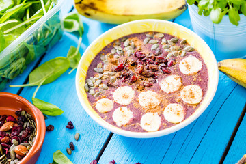 Blueberry Smoothie Bowl with Banana, Pumpkin Seeds, Cranberries and Cinnamon for Healthy Vegan Vegetarian Diet Breakfast on Blue Wooden Table, Horizontal View