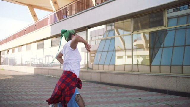 Attractive young woman in a stylish look and green hair dancing freely on urban background, slow motion