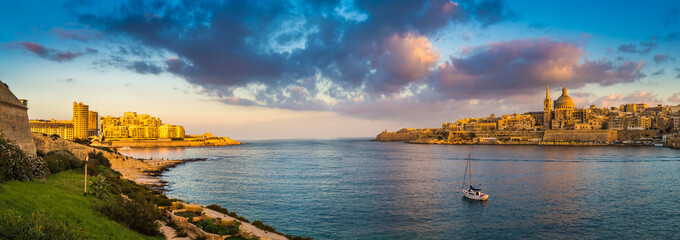 Valletta, Malta - Panoramic skyline view of the ancient city of Valletta and Sliema at sunrise shot from Manoel island at spring time with sailing boat, blue sky, beautiful clouds and green grass - obrazy, fototapety, plakaty