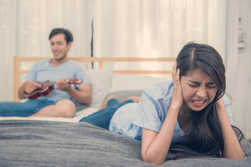 Young woman suffering with Noisy of man play ukulele song on bedroom