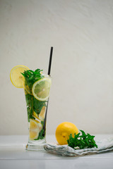 Healthy lemon and mint leaves detox water in cocktail glass on white wooden table with lemon and napkin by side. Non-alcoholic mojito or lemonade with ice cubes on white background