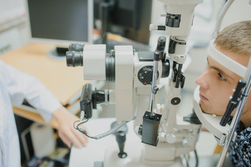Young beautiful two doctors /eye specialist/optometrist in an ophthalmologic clinic examines a woman patient with biomicroscopy