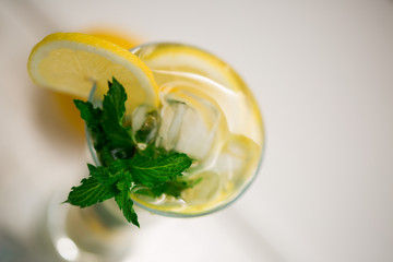 Healthy lemon and mint leaves detox water in cocktail glass on white wooden table with lemon and napkin by side. Non-alcoholic mojito or lemonade with ice cubes top view on white background