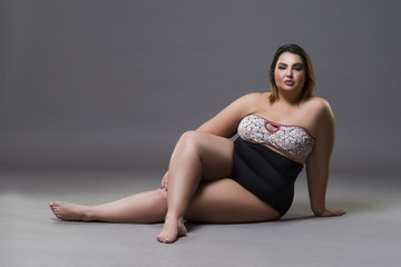 Plus size fashion model in sexy swimsuit, young fat woman on gray background, overweight female body