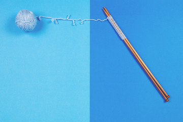 Knitting needles and blue yarn ball on blue background