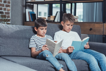 little caucasian boys reading books while sitting on sofa at home