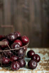 Ripe plums in a basket on a wooden background.