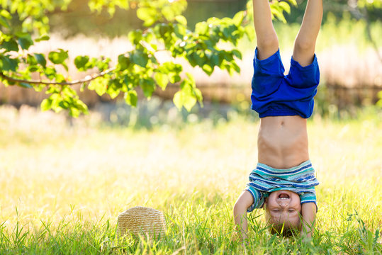 Boy standing upside down on his hands outdoor on the green grass
