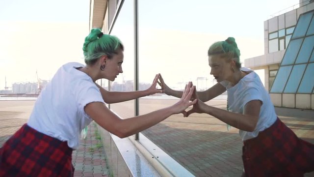 Attractive young woman in a stylish look and green hair dancing freely on urban background, slow motion