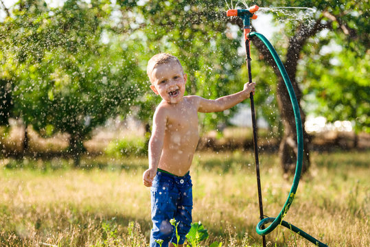 A boy play with water sprinkler in the summer garden