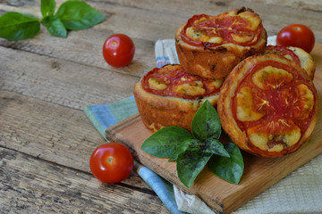 Salty snack. Homemade muffins with cheese, tomatoes and basil on wooden background. Savory pastry.